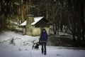 Woman walking alone towards a wooden cabin in the middle of a snowy forest Royalty Free Stock Photo