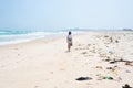Woman walking alone on tropical beach with rubbish trash plastic on sand. Waving ocean desert beach pollution problem in the sea. Royalty Free Stock Photo
