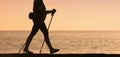 Woman walking along the shore with hiking poles