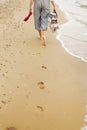 Woman walking barefoot on beach, back view of legs. Young girl relaxing on sandy beach, walking with shoes and bag in hands. Royalty Free Stock Photo