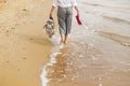 Woman walking barefoot on beach, back view of legs. Young girl relaxing on sandy beach, walking with shoes and bag in hands. Royalty Free Stock Photo
