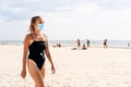 Woman walking on the beach wearing a face mask to protect from corona virus. Tourist on a vacation with people in the background.