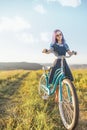 Woman walking with bicycle cruiser on countryside summer road.