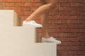 Woman is walking down white concrete stairs outside in the buildings with orange brick background. Royalty Free Stock Photo