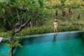 Woman walking on edge of pool and enjoy jungle view wearing beige bikini and hat. Vacation concept