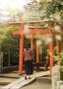 Woman walking at the entrance of a tunnel of red Torii portal in