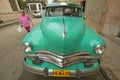 A woman walking in front of turquoise old Dodge parked in front of old buildings in Havana, Cuba