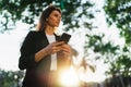 Woman walking outside in city park and hold in hand mobile phone chatting with friends sun day, businesswoman typing on touch Royalty Free Stock Photo