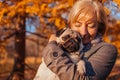 Woman walking pug dog in autumn park. Happy lady hugging pet. Best friends Royalty Free Stock Photo