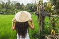 Woman walking in rice fields with traditional balinese straw hat in Ubud