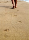 Woman walking on sand beach leaving footprints