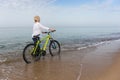 Woman walking in the sea wheeling a bicycle
