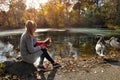 Woman walking with a small dog near beautiful lake with swans