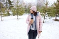 Woman walking on a snowy path in winter with a cup of drink in a forest setting Royalty Free Stock Photo