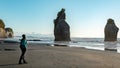 Woman walking in Three Sisters rock formations, coast of New Plymouth, New Zealand. You can see Mount Taranaki behind