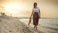 Woman walking towards the sunset on a sandy sea beach, holding a silk scarf and capturing the essence of happiness and positivity