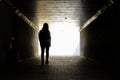 Woman walking through a tunnel in the dark with light at the end Royalty Free Stock Photo