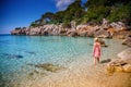 A woman walking in the water on Cala Gat beach in Mallorca, wearing a summer dress and straw hat