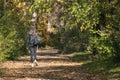 Woman walks along an alley with fallen leaves. Lonely young woman with dark hair walk through the forest. Back view