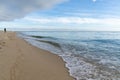 Woman walks along an endless golden sand beach with gentle waves Royalty Free Stock Photo