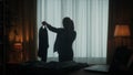 A woman walks around the room and speaks on the phone. A woman holds a blouse on a hanger in her hand. Dark silhouette