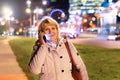 A woman with a mobile phone in her hand is walking through the night city