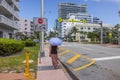 Woman walks down Collins Avenue on scorching, sunny day, shielding herself from sun\'s rays with UV-protective umbrella.