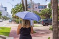 Woman walks down street, shielding herself from scorching sun with UV-protective umbrella.