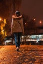 Woman walks at night in an autumn park. Rear view of young female in white coat walking away on wet alley Royalty Free Stock Photo