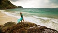 Woman walks on rock of sea reef stone, stormy cloudy ocean. Blue swimsuit dress tunic. Concept rest, tropical resort Royalty Free Stock Photo