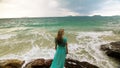 Woman walks on rock of sea reef stone, stormy cloudy ocean. Blue swimsuit dress tunic. Concept rest, tropical resort Royalty Free Stock Photo