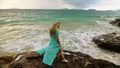 Woman walks on rock of sea reef stone, stormy cloudy ocean. Blue swimsuit dress tunic. Concept rest, tropical resort Royalty Free Stock Photo