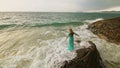 Woman walks on rock of sea reef stone, stormy cloudy ocean. Blue swimsuit dress tunic. Concept rest, tropical resort Royalty Free Stock Photo