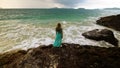 Woman walks on rock of sea reef stone, stormy cloudy ocean. Blue swimsuit dress tunic. Concept rest, tropical resort Royalty Free Stock Photo