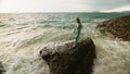 Woman walks on rock of sea reef stone, stormy cloudy ocean. Blue swimsuit dress tunic. Concept rest, tropical resort Royalty Free Stock Photo