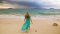 Woman walks to the stormy cloudy ocean on sand beach. Girl in blue swimsuit dress tunic. Concept rest in sea, tropical Royalty Free Stock Photo