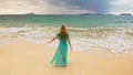 Woman walks to the stormy cloudy ocean on sand beach. Girl in blue swimsuit dress tunic. Concept rest in sea, tropical Royalty Free Stock Photo