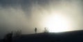 A woman walks towards the sun in the blown fog on top of a mountain on a cold winter day in southern France Royalty Free Stock Photo