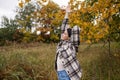 A woman in warm clothes in the autumn forest raised her hands up to stretch