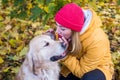 Woman in warm clothes whispers something in the ear of a retriever among autumn yellow leaves