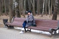 A woman in warm clothes and white sneakers sits on an old wooden bench in a park Royalty Free Stock Photo
