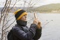 A woman in a warm jacket photographs nature in late autumn. dressed in a yellow hat, takes pictures of nature and