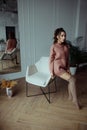 A woman in a warm pink sweater and knee socks is sitting on the back of a chair.