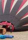 A woman in warm winter clothes watches as a red white and black hot air balloon fills in preparation for lift off