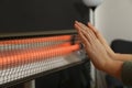 Woman warming hands near electric infrared heater indoors, closeup Royalty Free Stock Photo