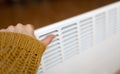 Woman warming her hand on a warm electric heater, saving energy, heating season concept