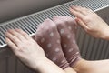 A woman warms her feet and hands on a radiator