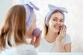 Woman washes her face with natural sponge and soap scrub cosmetic foam in bathroom portrait reflection in mirror Royalty Free Stock Photo