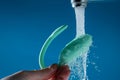 A woman washes a vibrator under running water on a blue background. Women's Health Kegel Trainer.