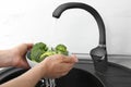 Woman washing bowl of fresh green broccoli in kitchen sink, closeup